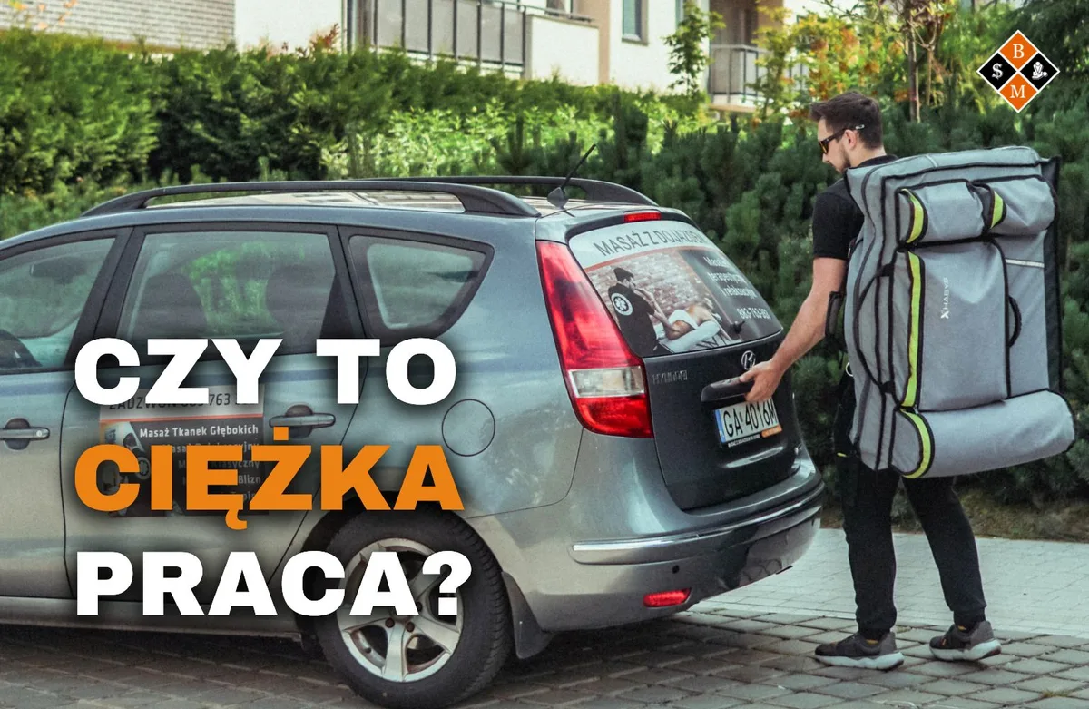 Masażysta z torbą na stół przy aucie z reklamą masażu, napis „Czy to ciężka praca?”