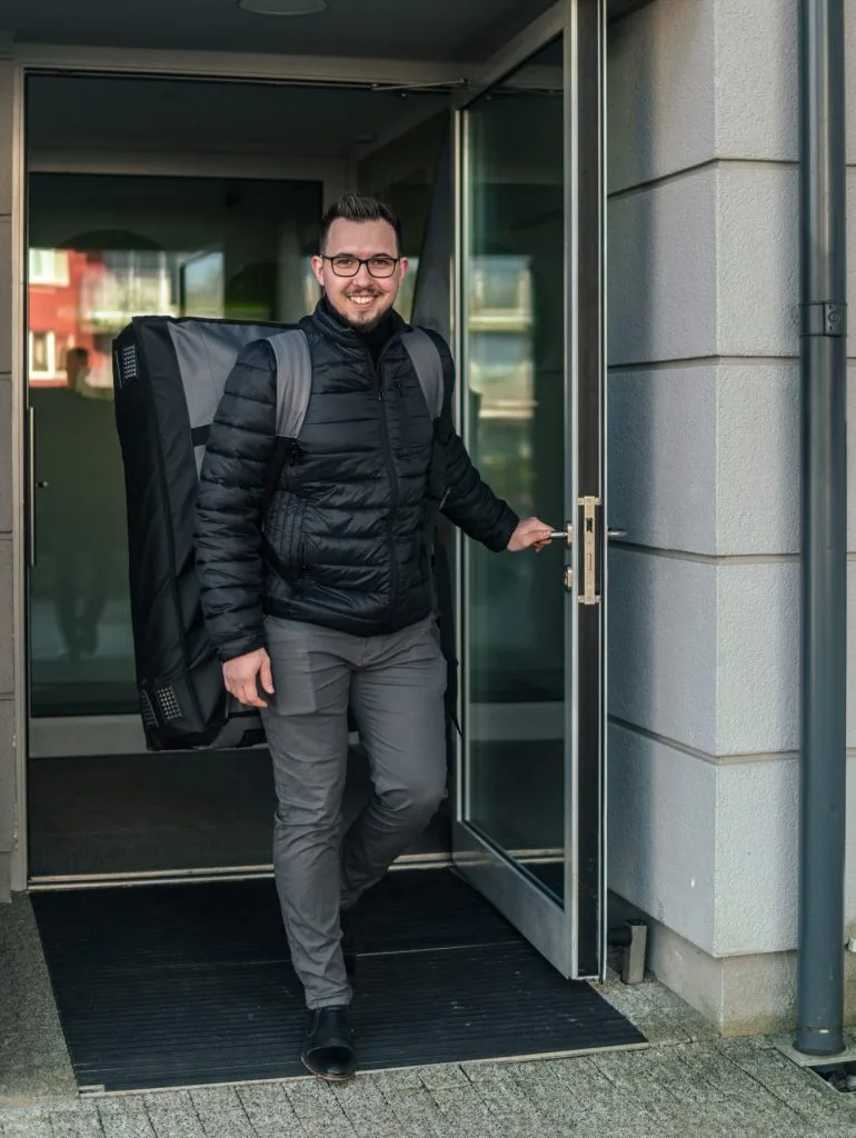 Masażysta mobilny wychodzi z budynku ze stołem do masażu w pokrowcu na plecach