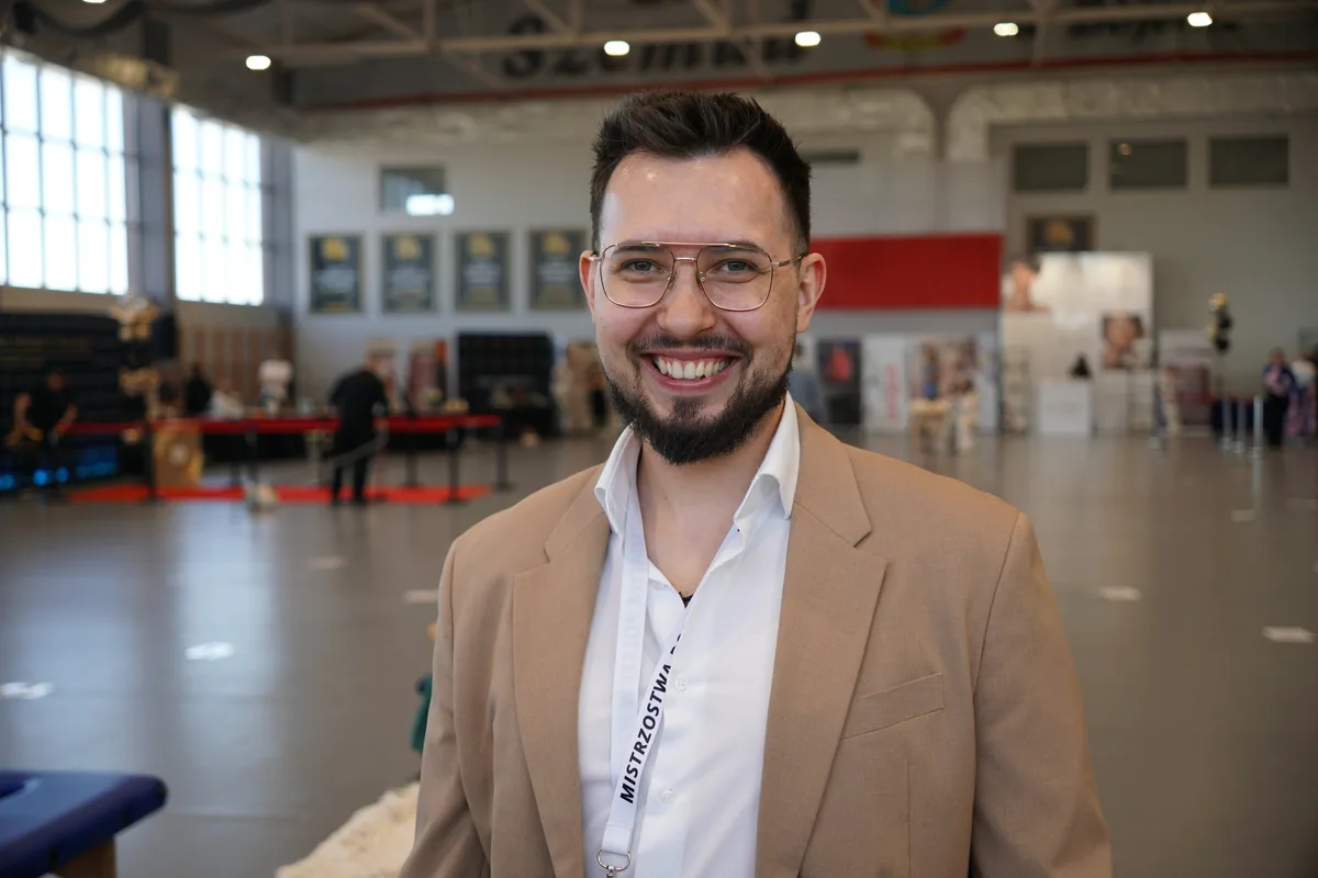 Uśmiechnięty uczestnik Mistrzostw Polski w Masażu z identyfikatorem na hali sportowej